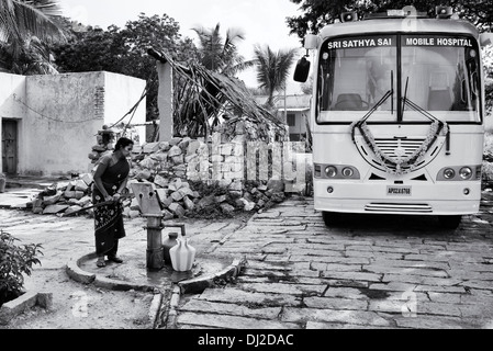 Indianerdorf Frau Wasser aus einer Hand-Pumpe vor Sathya Sai mobiles Krankenhaus Bus Topf einfüllen. Andhra Pradesh, Indien Stockfoto