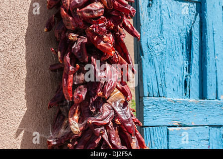 Eine rote Chile Pfeffer Girlanden hängt trocknen in der Sonne auf einer Adobe-Wand neben eine leichte blaue verwitterten Holztüre in Santa Fe, nm Stockfoto