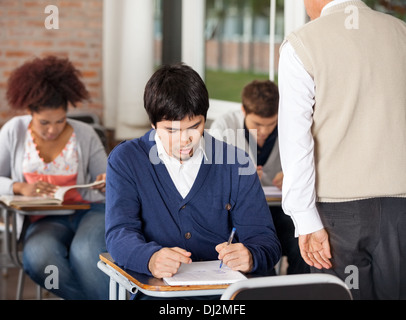 Studenten geben Prüfung während Lehrer im Klassenzimmer Aufsicht Stockfoto