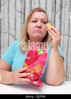 Übergewichtige Frau, die einen Beutel mit Familie-große Chips zu essen. Stockfoto