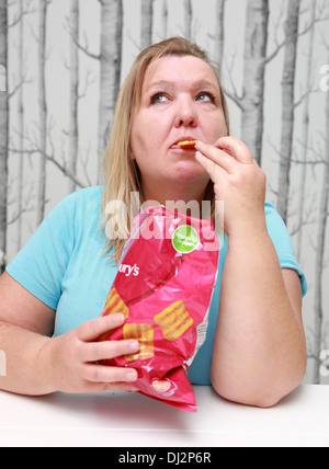 Übergewichtige Frau, die einen Beutel mit Familie-große Chips zu essen. Stockfoto