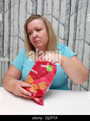 Übergewichtige Frau, die einen Beutel mit Familie-große Chips zu essen. Stockfoto