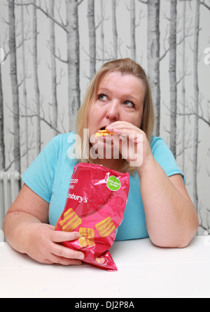 Übergewichtige Frau, die einen Beutel mit Familie-große Chips zu essen. Stockfoto