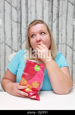 Übergewichtige Frau, die einen Beutel mit Familie-große Chips zu essen. Stockfoto