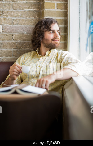 Mann mit Kaffeetasse Blick durch Fenster im Cafe Stockfoto