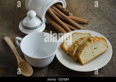 Scheiben-Bananen-Kuchen auf Teller, Zimtstangen und leere Tasse mit Löffel Stockfoto