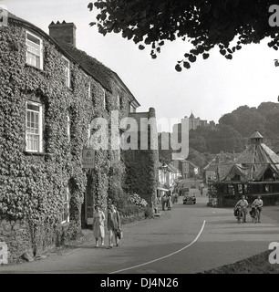 1950s, historisches Bild aus dieser Zeit mit Blick auf die Hauptstraße von Dunster, einem Dorf aus dem Mittelalter und mit antikem Schloss, Priorat, Dovecote, Garnmarkt, Gasthäusern und Teestuben in Somerset, im Südwesten Englands, Großbritannien. Dunster Castle ist in der Ferne zu sehen. Stockfoto