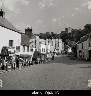 Historical, 1950s, Dunster High Street. Dunster ist ein altes Dorf aus dem Mittelalter, mit einer alten Burg - im Hintergrund gesehen - Priorat, Dovecote, Garnmarkt, Gasthäusern und Teestuben in Somerset, England. Stockfoto