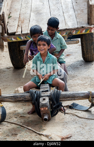 Indischen Jungen spielen mit Stöcken auf einem Ochsenkarren in einem indischen Dorf. Andhra Pradesh, Indien Stockfoto