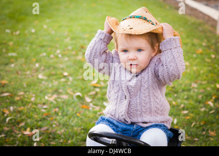 Glückliche junge Kleinkind tragen Cowboyhut und auf Spielzeug-Traktor draußen spielen. Stockfoto