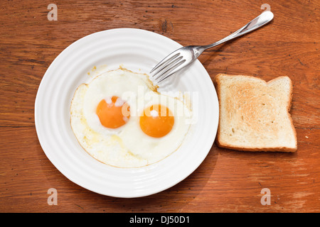 Frühstück mit zwei Spiegeleier auf weißen Teller, frischen Toast auf Holztisch Stockfoto