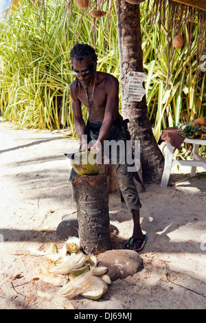 Obstverkäufer am Strand von Guadeloupe peeling eine Kokosnuss mit einer machete Stockfoto