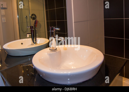 Eine Detailansicht eines modernen Badezimmer-Zählers mit Spüle, Wasserhahn und großer Spiegel an der Wand. Stockfoto