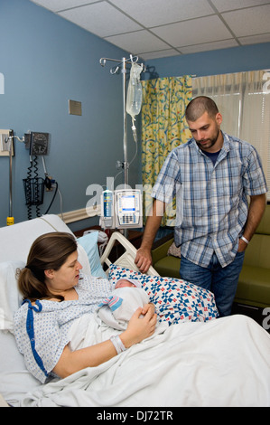 Frau hält ihr neugeborenes Baby im Krankenhaus während Ehemann Uhren Stockfoto