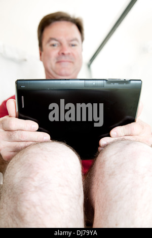 Mann mit seinem TabletPC im Bad auf der Toilette sitzend. Stockfoto