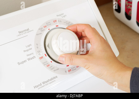 Horizontale Foto von weiblicher Hand Dial-on-Waschmaschine mit Wäschekorb im Hintergrund anpassen Stockfoto