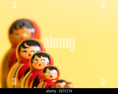 Gruppe von russischen Matroschka Puppen in einer Reihe mit selektiven Fokus auf eine Puppe, umrahmt von einem hellgelben Hintergrund. Stockfoto