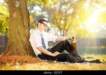 Enttäuscht junger Mann sitzt auf einer Wiese mit Flasche in der Hand, im park Stockfoto