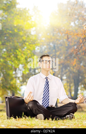 Junge Unternehmer sitzen auf einem grünen Rasen meditierend in einem park Stockfoto