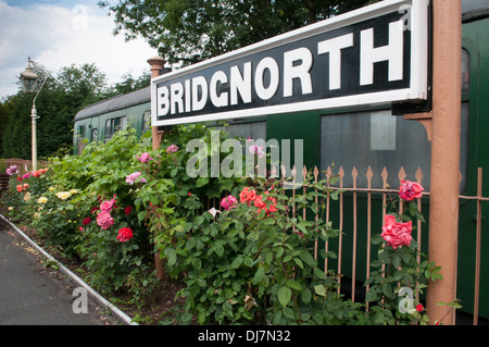 Schwarz und weiß aus Gusseisen Plattform Schild für Bridgnorth am Severn Valley Railway über eine ordentlich rose Grenze Stockfoto