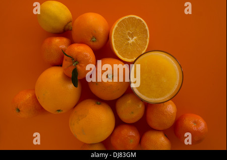 Eine Gruppe von Zitrusfrüchten und ein Glas Saft über einem orangefarbenen Hintergrund Stockfoto