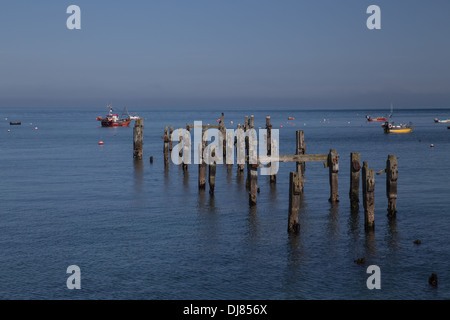 Swanage Bay, Dorset, England. Ruhiges Meer und blauer Himmel. Alte Mole im Vordergrund. Boote vor Anker in Ferne. Stockfoto