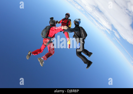 Dieser Fallschirmspringer-Team ist in den blauen Himmel Kopf fliegen vorbei. Sie halten Hand und bilden eine Sternentstehung zusammen über den Wolken. Stockfoto