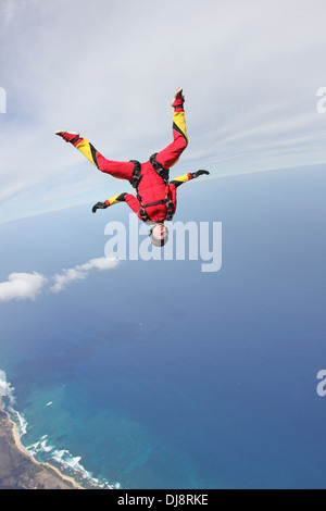 Dieses Fallschirmspringer Mädchen fliegt in einem Kopf nach unten über das tiefblaue Meer neben der Uferlinie mit hoher Geschwindigkeit von 130 km/h. Stockfoto