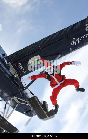 Dieser Fallschirmspringer in ein Weihnachtsmann-Kostüm springt aus einem Flugzeug in einer Position sitzen auf den blauen Himmel. Stockfoto