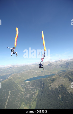 Fallschirmspringer mit bunten Luftschläuche und Freunde fallen durch den blauen Himmel über Berge mit einem See in den Boden zurück. Stockfoto