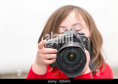Junges Mädchen mit Down-Syndrom, posiert mit einer Canon 20 D Kamera vor einem weißen Hintergrund. Stockfoto