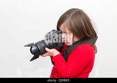 Junges Mädchen mit Down-Syndrom, posiert mit einer Canon 20 D Kamera vor einem weißen Hintergrund. Stockfoto