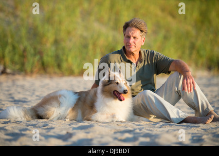 Kaukasischen Mann, sitzend mit Hund am Strand Stockfoto