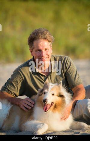 Kaukasischen Mann, sitzend mit Hund am Strand Stockfoto