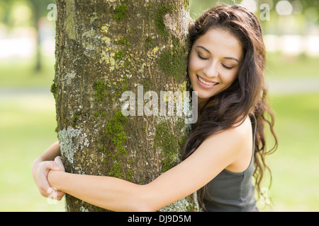 Lässige fröhlich Brünette umarmt einen Baum mit geschlossenen Augen Stockfoto