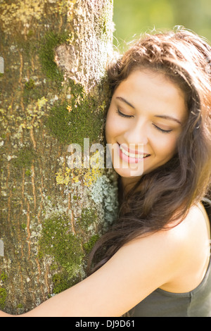 Lässig lächelnd Brünette umarmt einen Baum mit geschlossenen Augen Stockfoto