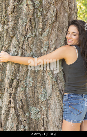 Lässige schöne Brünette umarmt einen Baum mit geschlossenen Augen Stockfoto