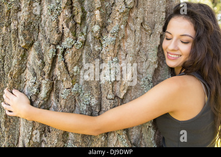 Lässige wunderschöne Brünette umarmt einen Baum mit geschlossenen Augen Stockfoto