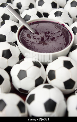 Brasilianischer Kultur auf dem Tisch verfügt über eine Schüssel mit frischen Acai umgeben von Fußball Fußbälle Stockfoto