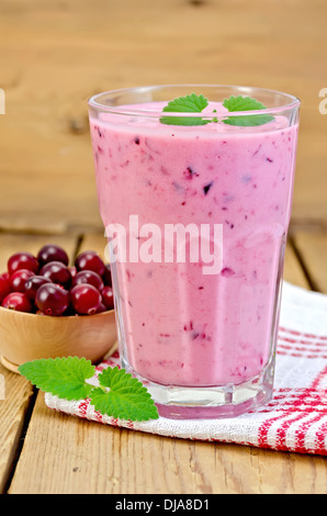 Milch-Cocktail mit Preiselbeeren in einem Glas auf einer Serviette, Tasse Preiselbeeren, Minze auf dem Hintergrund der Holzbretter Stockfoto