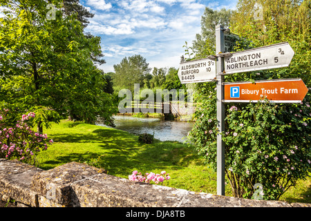 Blick über den Fluss Coln in Bibury mit einem Wegweiser nach anderen Cotswold-Städte und Dörfer und der Forellenzucht. Stockfoto