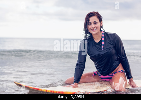 Schöne junge Frau sitzt auf Surfbrett im Wasser Stockfoto