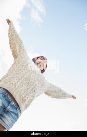 Frau im weißen Pullover und Jeans-Shorts, streckte ihre Arme gegen Himmel Stockfoto