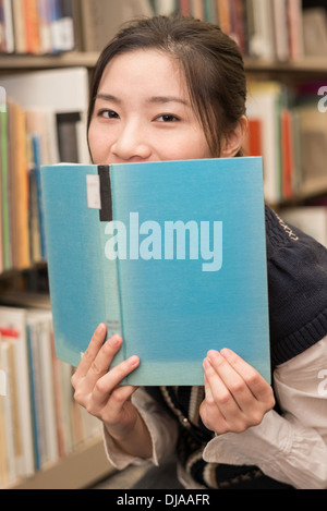 Verspielte Studentin den Mund mit einem blauen Hardcover-Buch in Bibliothek