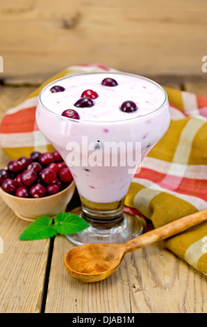 Dicken Joghurt im Glas mit Löffel, Serviette, Cranberries, Preiselbeeren in einer Schüssel, Minze auf Holzbrettern Hintergrund Stockfoto