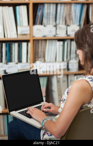 Seitenansicht eines weiblichen Studenten gegen Bücherregal mit Laptop in der Bibliothek Stockfoto