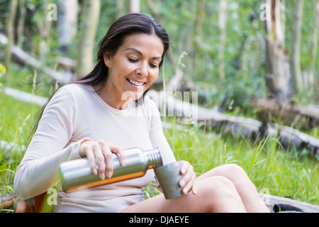 Hispanic Frau Gießen Tasse Kaffee im Wald Stockfoto