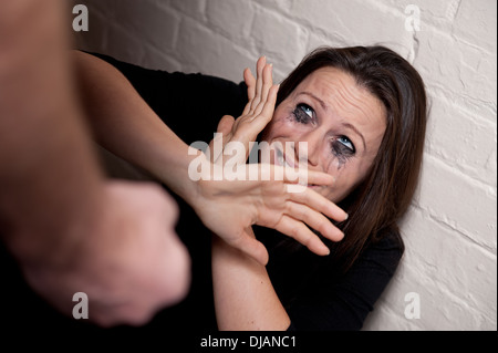 Häusliche Gewalt-junge Frau gegen eine weiße Wand, die versuchen, sich von einem Mann zu schützen die Faust geballt. Stockfoto