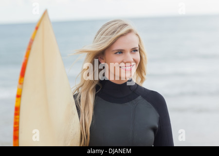 Lächelnde Frau in Neoprenanzug mit Surfbrett am Strand Stockfoto