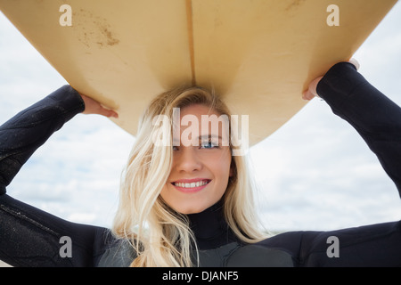 Lächelnde Frau in Neoprenanzug Surfbrett über den Kopf halten Stockfoto